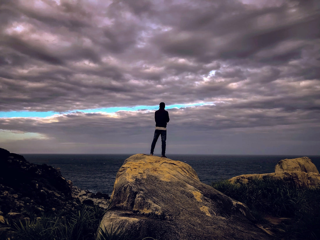 silhouette of person standing on rock formation during sunset