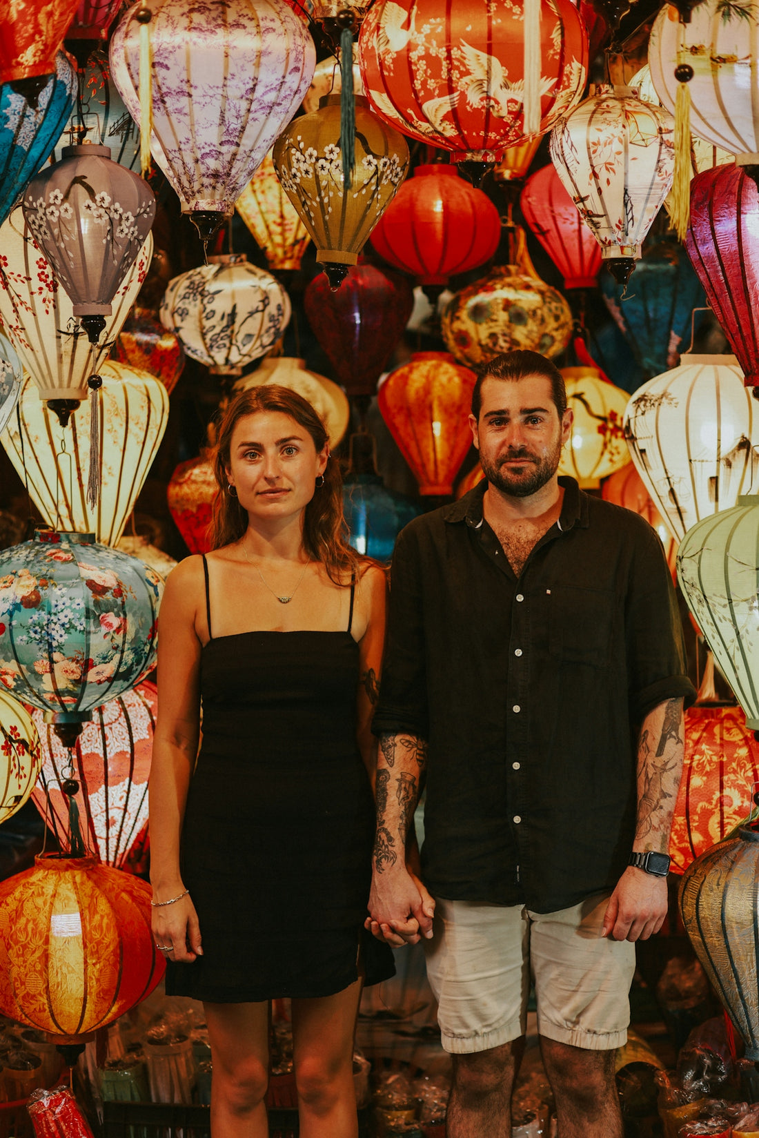 a man and a woman standing in front of a wall of lanterns