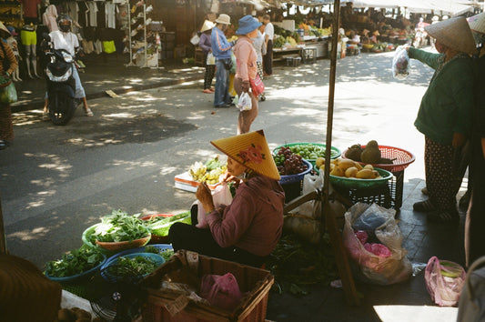 Woman in conical hat sells produce at market.